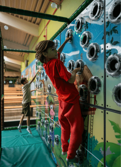 Child in red jumpsuit climbing on jungle theme trailblazer climbing wall